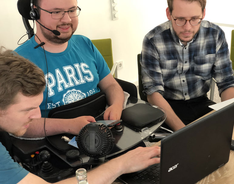 Proband mit Muskelschwunderkrankung, Testleiter und Assistent vor Laptop