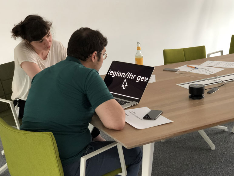 Testsituation: Proband mit Seheinschränkung arbeitet mit starker Vergrößerung, Testleiterin schaut interessiert zu.