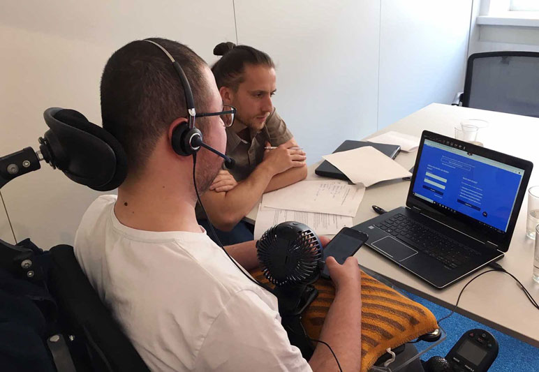 Testsituation: Testleiter und Proband im Rollstuhl betrachten einen Laptop-Bildschirm
